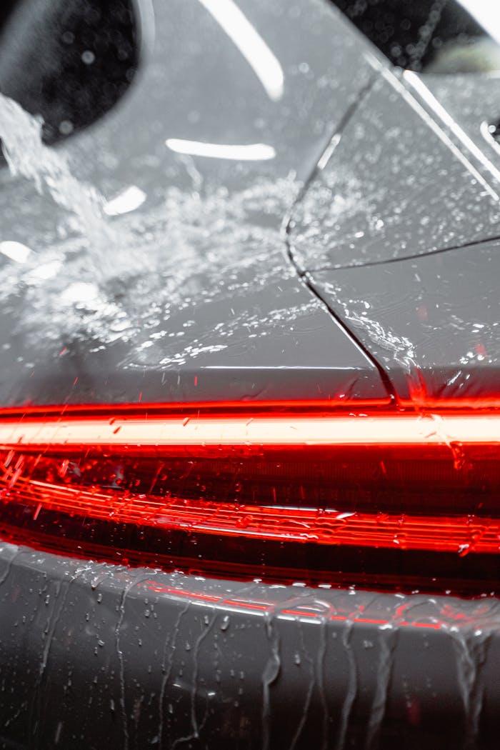Close-up of a vehicle's taillight being washed, featuring water and soap suds for a clean and shiny finish.
